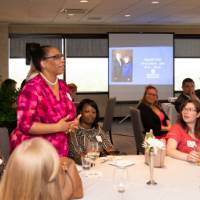 woman at table stands to address tom and marcia